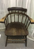 Front view of antique Windsor chair showing curved rounded backrest, spindles, and wooden seat with wear.