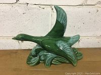 Front angle of vintage green ceramic duck lamp on wooden surface with white brick wall background.