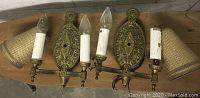 Photo of pair of brass wall sconces with two candle sleeve bulbs each, displayed with the matching woven lampshades lying next to them on a wooden surface.