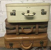 Full view of three vintage suitcases stacked, showing colors, materials, and hardware