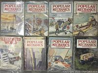 Eight vintage magazines arranged closely together. Seven Popular Mechanics magazines with illustrated covers, one Illustrated World magazine also with illustrated cover featuring a tank scene.