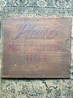 Front of wooden sign showing faded painted text 'Please No Standing Here'.