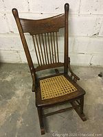 Front angle view of antique child-sized rocking chair, showing wood frame and cane seat.