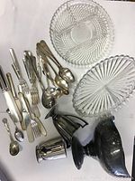 Overview of the lot showing the two clear glass dishes, assorted silverplate knives, forks, spoons, a small creamer, goblet, and a large footed bowl