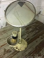Full view of vintage barber mirror mounted on metal stand with chipped paint and shaving brush in bowl holder attached to base.