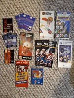 Photo of various NHL schedules and related hockey collectibles arranged on carpeted floor showing multiple pamphlets, pin sets, and cards.