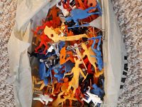 Plastic figures in mixed colors including orange, blue, white, and yellow, depicting Vikings, knights, Zulus, and other soldiers inside a white sack.