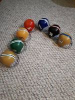 Seven miniature CFL helmets from early 1980s Dairy Queen promotion placed on a carpeted floor showing different team logos and colors.