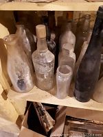 Shelf with assorted antique bottles including clear and black glass with visible residue and wear