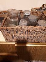 Photo showing several vintage glass canning jars of various sizes with metal lids inside a large woven wicker box labeled Shannonville Canning Factory.