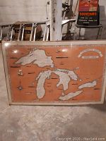 Great Lakes Shipwreck Chart in original packaging leaning against a wall in a basement or storage area. Orange and white color scheme with shipwreck illustrations in the Great Lakes area.