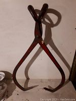 Front view of large antique ice tongs showing curved hooked ends and red paint with wear.