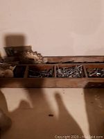 Wooden tray with multiple compartments filled with assorted screws, bolts, nuts, and washers