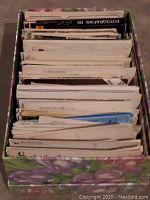Box filled with a large set of postcards stored upright showing edges and some text on the backs of cards.