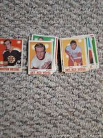 Photo showing a spread of about 20 hockey trading cards from the 1970-71 O-Pee-Chee NHL series laid out on a carpet, featuring players from Boston Bruins, Detroit Red Wings, and others.