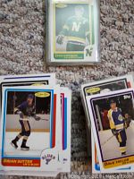 Pile of hockey cards with Craig Hartsburg card shown on top in protective sleeve, other cards include Brian Sutter and Dave Taylor visible.