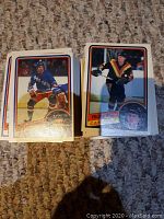 Two stacks of hockey cards showing front of cards with players in action on ice, including a New York Rangers player and Vancouver Canucks player, clear card fronts with vibrant colors and minor wear.