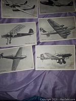 Photo showing six WWII airplane illustrated collectible cards laid flat on a purple fabric surface. The cards depict German aircraft like the Fieseler Fi 156 Storch, Junkers Ju 52/3m, and other planes with German markings.