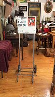 Full view of the vintage metal dolly cart with attached 7Up promotional sign in a room setting with wooden floor and various antiques around.