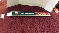 Full view of the Orange Crush push bar lying on a patterned red cloth background, showing the entire bar with logo and slogan.
