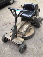 Angle view of the Craftsman ride-on lawn mower showing the black cushioned seat, steering handle, and front tires with one misaligned tire.