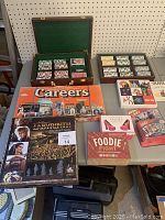 Full overview of all board games, card games, and poker chips in a wooden case with green felt lining. Visible are 2 decks of cards and many clay poker chips in multiple colors. The latch on the poker chip case is broken.