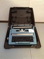 Robins egg blue Smith-Corona Electra XT electric typewriter inside open black hard carrying case showing full front and keyboard.