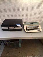 Mid-century Royal typewriter and black hard case on tabletop against pegboard background.