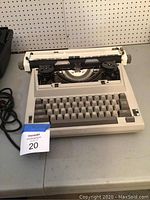 Front view of the vintage electric SR 1000 typewriter showing the keyboard, power cord, and ribbon spools.