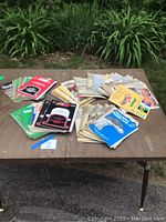 Photo showing a large assortment of vintage dog racing programs spread out on a table outdoors, with greenery in the background.