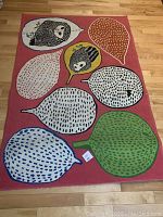 Top view of pink playroom rug with colorful leaf and owl face motifs laid on wooden floor.