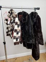 Three vintage faux fur coats hung on a metal clothing rack, showing full length and texture differences
