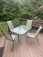 Full view of the outdoor dining set on deck, includes rectangular glass table with metal frame and 4 matching metal mesh chairs