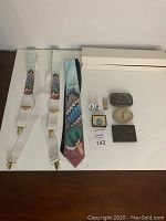 Front view of all items laid out on a flat surface showing suspenders, ties, belt buckles, cufflinks, tie tack, and money clip.