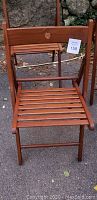 Front view of one wooden folding chair stained in cherry wood tone showing slatted seat and backrest with hole for hanging.