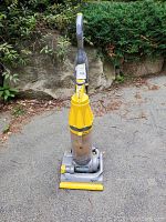 Front view of Dyson DC07 upright vacuum showing yellow top and base, clear dust bin, gray handle and hose attached.