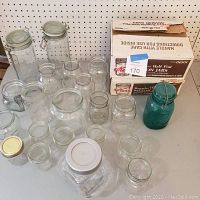 Large lot of assorted clear glass canning jars, including wide-mouth jars, some with clamp lids, and a distinctive bright blue glass Ball jar on the right side.