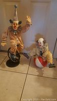 Both clown figurines shown side by side on a tiled floor, one on a unicycle and other on a ball, showing condition and scale.