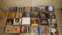 Four rows of mixed-genre CD jewel cases arranged on floor against door.