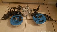 Lot of three Westcott Spiderlite TD5 continuous lighting heads with blue control units and coiled power cords on tiled floor.