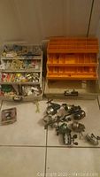 Overview of 9 fishing reels alongside two tackle boxes, one full and beige, one empty and orange.