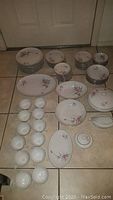 Full view of the 80 piece fine china set laid out on floor, grouped by plates, bowls, cups, and serving pieces.