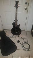 Full front view of black Dean Playmate electric guitar on stand, showing body, neck, and black gig bag on floor.