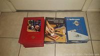 Photo showing three stacks of books including red covered woodworking books, a Sharpening and Tool Care book, and blue books on Bathrooms from home repair series.