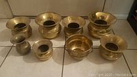 Eight brass spittoons arranged on tiled floor, viewed frontally.