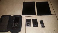 Overview photo shows two black iPads and three iPods of varying models and colors placed on tiled floor.
