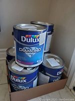 Six cans of Dulux Diamond white matte paint stacked together in a box, labels visible.