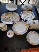 Melamine dinnerware set with floral pattern showing bowls, plates, saucers, and serving trays along with some spoons on black table surface
