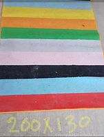 Close-up photo of the rainbow striped carpet showing colors and size 200x130 cm written on the carpet edge