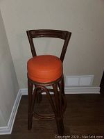 Single bar chair against wall showing wooden frame and orange round cushion seat